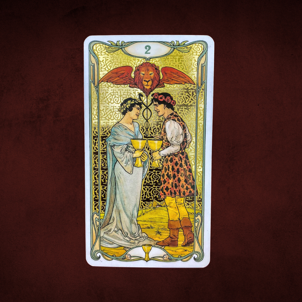 Tarot card with two people holding cups against a lion emblem on a dark brown background